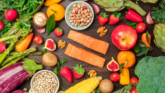 Foto von frischem Gemüse, Obst, Hülsenfrüchten und Fisch, gesunden Ernährungszutaten, von oben auf einer dunklen rustikalen Textur